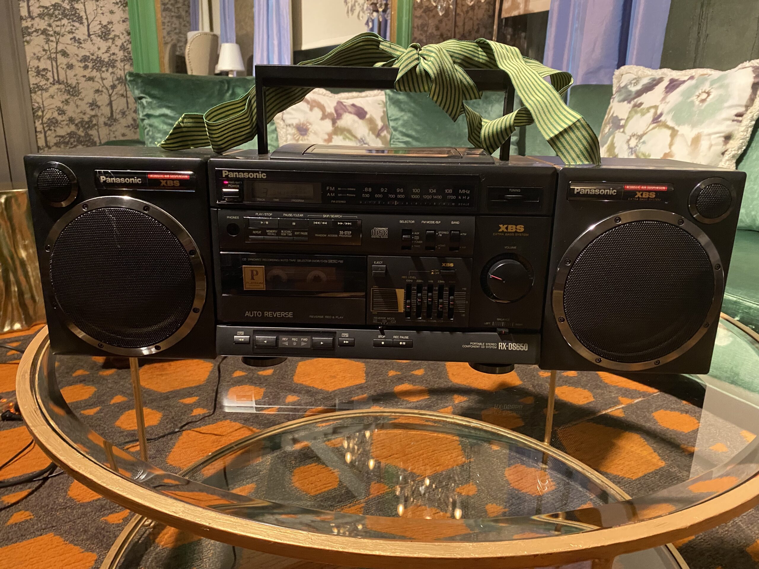 A Panasonic Rx-ds650 boombox sitting on a glass coffee table, with a green bow on top.