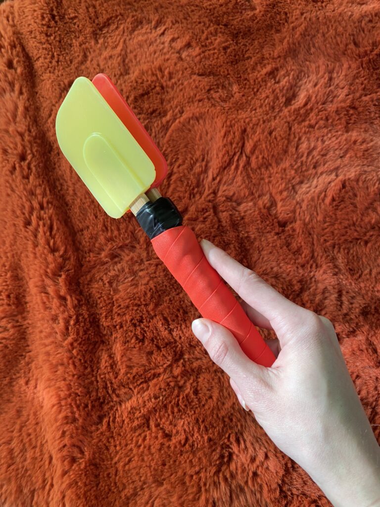 A paddle made from two kitchen spatulas in red and yellow rubber, with a wrapped foam grip.