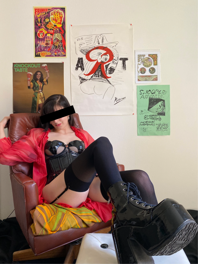a photo of me lounging in a chair with posters behind me. I'm wearing lingerie and my big PVC boots